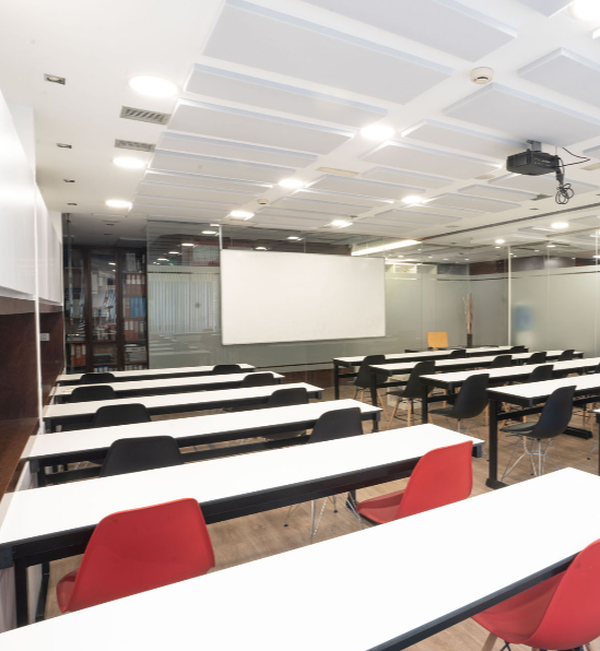 Aula amplia y moderna con mesas blancas y sillas de colores en una academia de oposiciones.