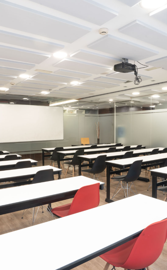 Aula de formación en Donostia preparada para clases de oposiciones de Correos, con mesas, sillas y proyector.